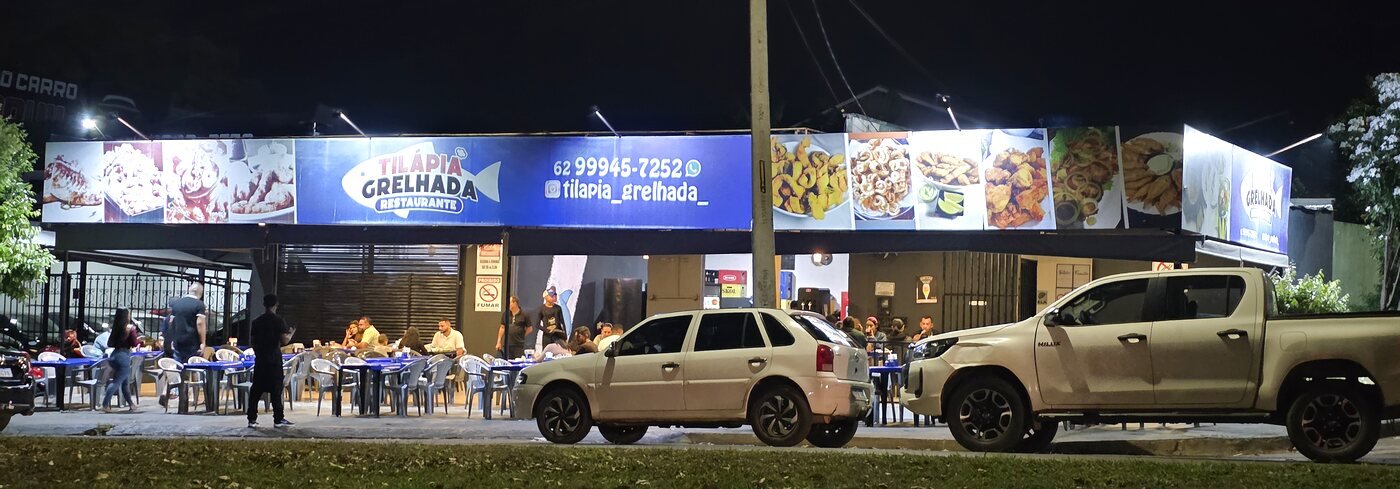 Fachada do restaurante Tilápia Grelhada à noite, com mesas e movimento